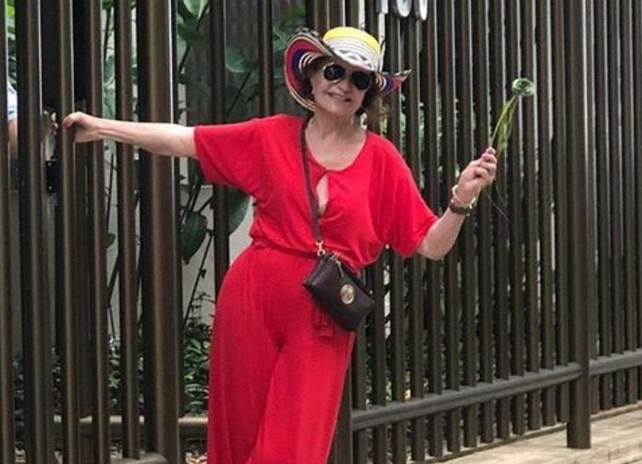 A atriz Rosamaria Murtinho posa com um macacão rosa, chapéuu e óculos de sol 