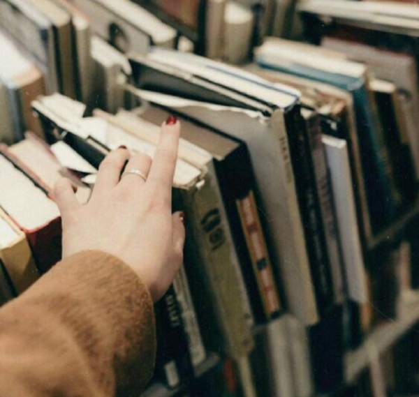 mão feminina sobre livros em uma estante