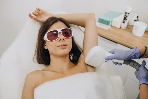 mulher usando óculos deitada em uma maca e fazendo depilação a laser na axila