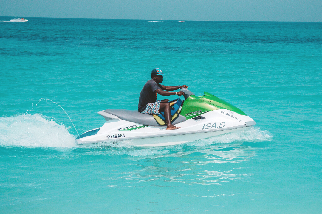 Imagem de um homem em cima de um Jet Ski branco e verde em uma praia paradisíaca.
