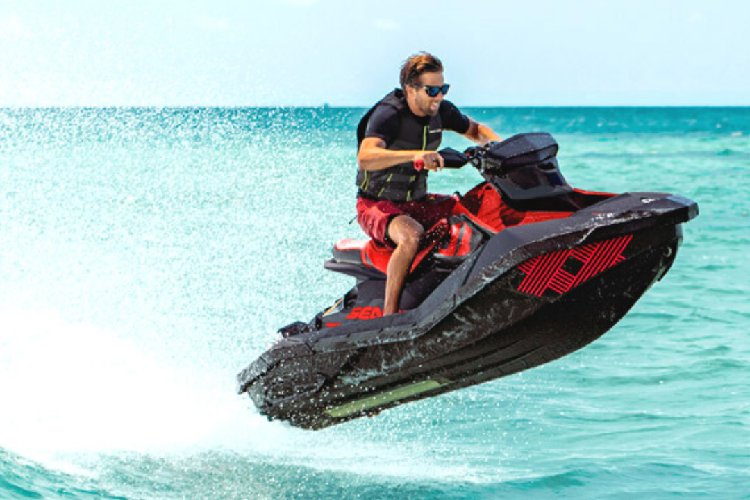 Imagem de um homem fazendo manobra em um Spark Trixx preto e vermelho em uma praia paradisíaca.