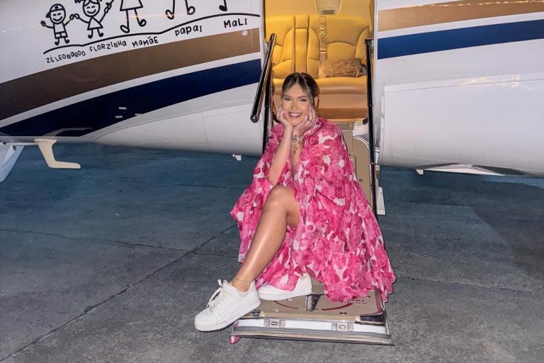 Virgínia Fonseca de vestido rosa e tênis branco sentada na escada de jatinho da família