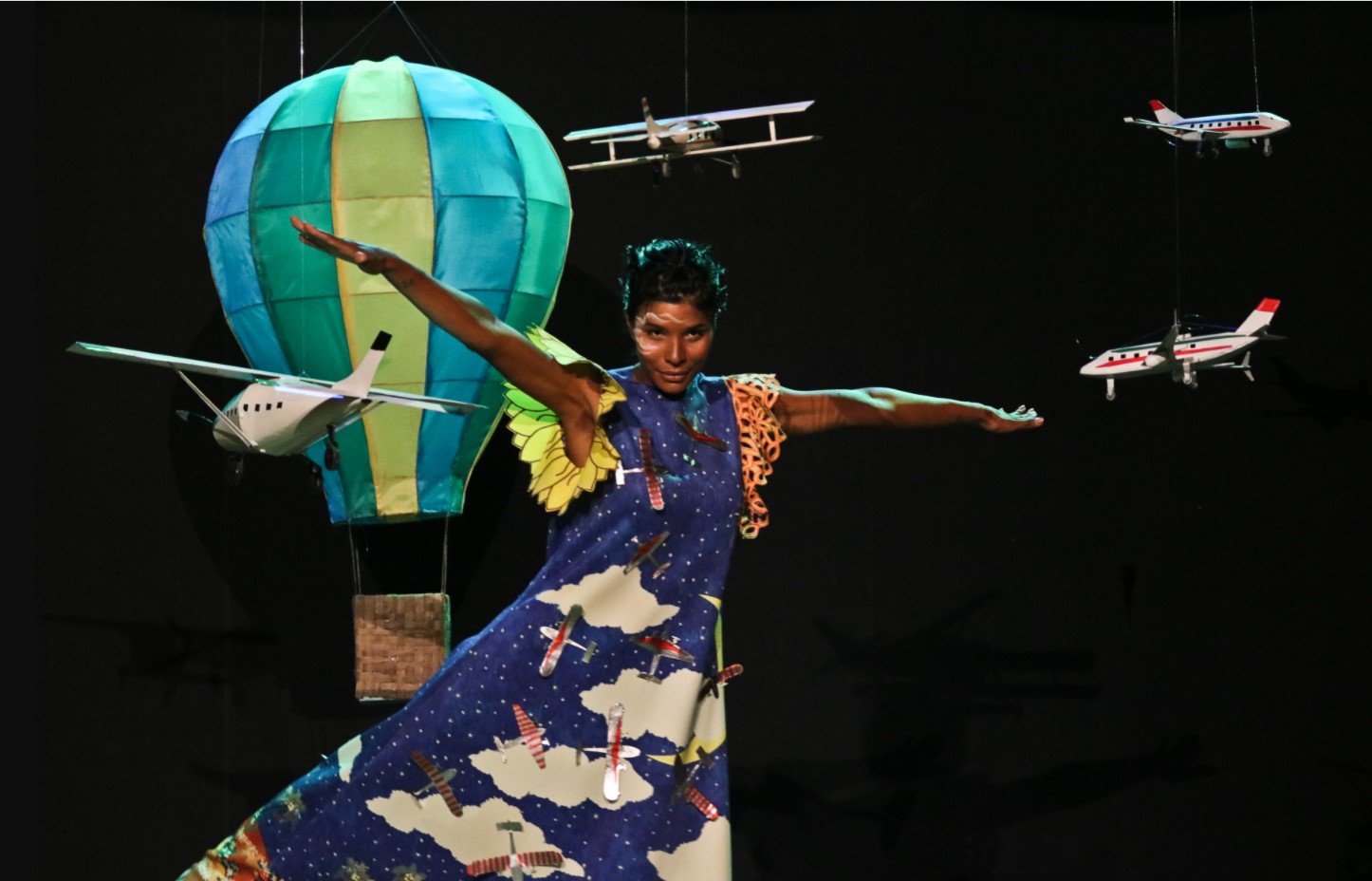 Modelo vestindo vestido azul, posando com aviões e um balão miniaturas.