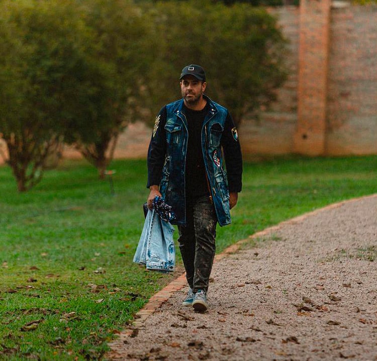 A foto do empresário João Foltran andando por um parque, carregando um par de jeans na mão esquerda.