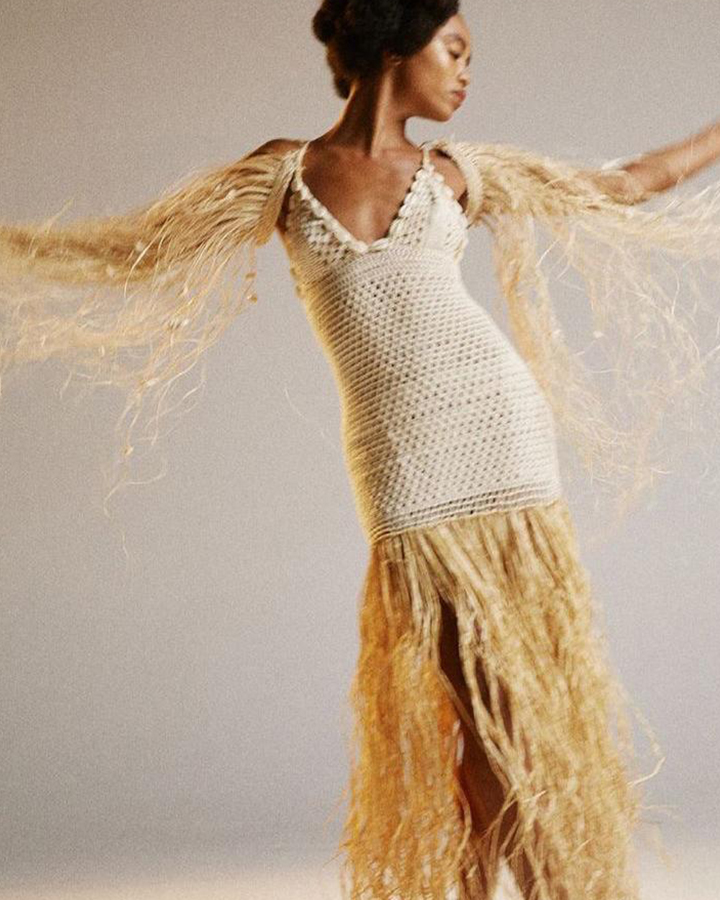 Modelo com um vestido de tricot bege com detalhes em palha.