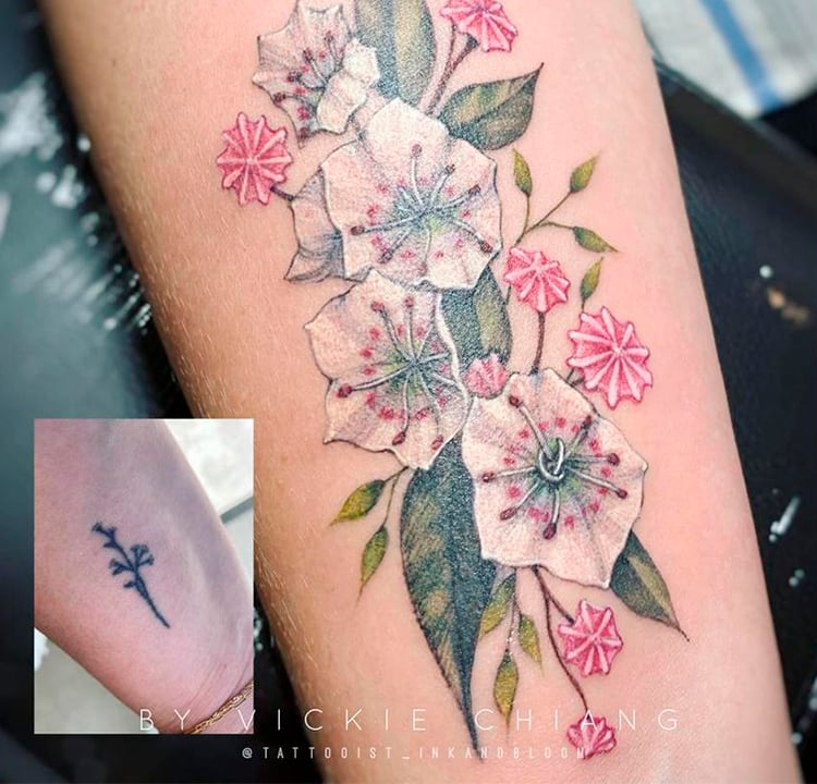 Tatuagem de flores coloridas cobre uma antiga e menor de flores pretas.
