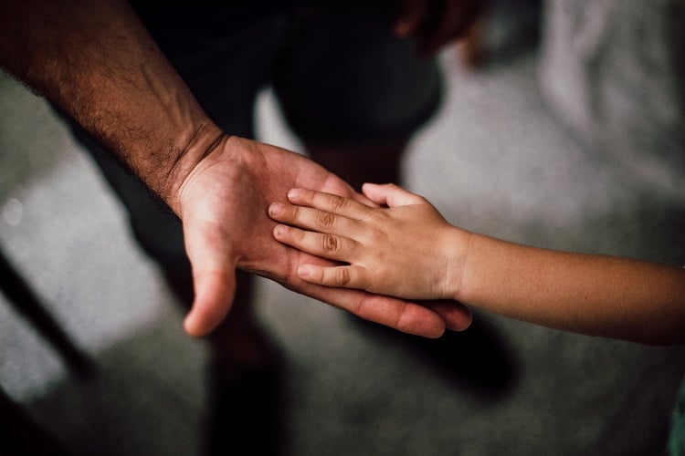 Foto de mão de um pai aberta, com a mão de seu filho por cima