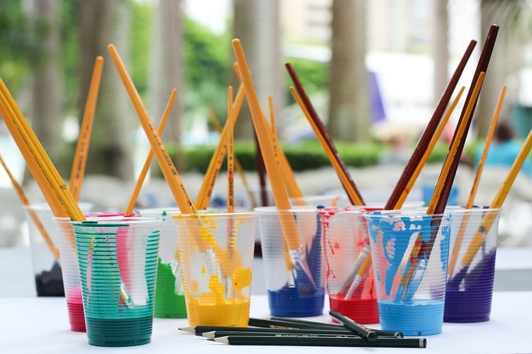 Foto de vários copos de plástico com tinta colorida e pincel dentro