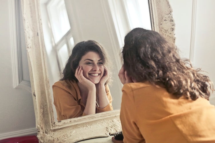 Foto de mulher sorridente com mãos no queixo se olhando no espelho
