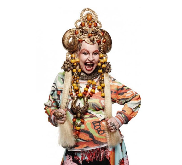 Elke Maravilha posando para a campanha de inverno 2015 da grife mineira Lucas Magalhães com uma roupa muito colorida, peruca loira muito longa, muitos acessórios, e um adorno na cabeça com chifres. 