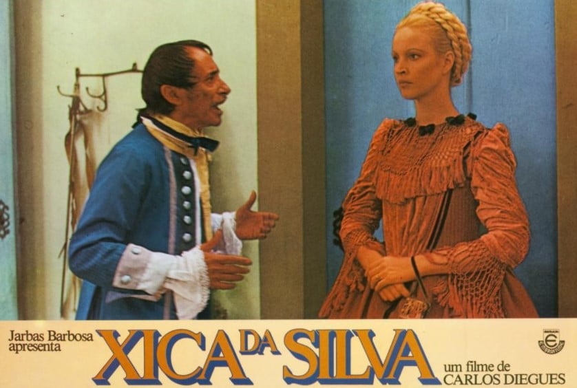 Cartaz com a cena do filme "Xica da Silva", onde aparece Elke vestida com um traje de época vermelho e cabelo longo preso com tranças no topo de cabeça.