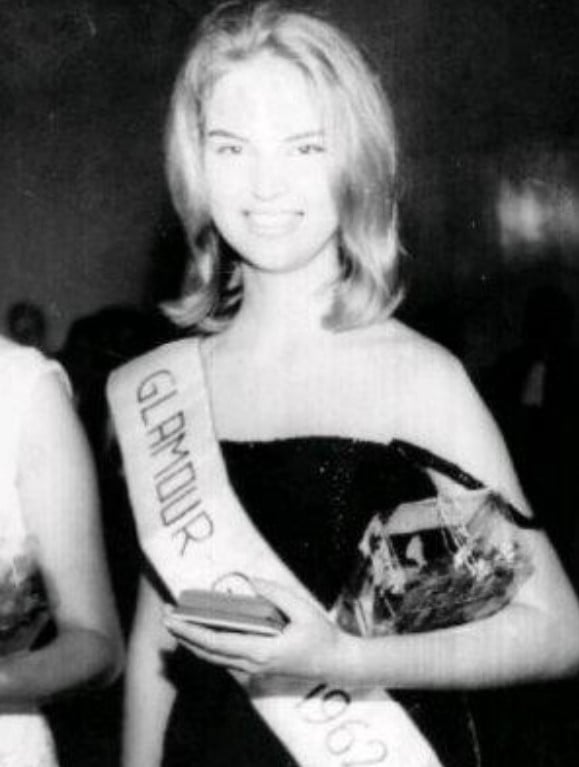 Foto em preto e branco de Elke Maravilha jovem, com um vestido preto e sorrindo ao usar uma faixa de Glamour Girl 1962.