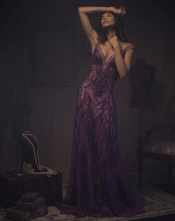 Modelo posando em pé com um vestido de festa de renda roxo de Ivanildo Nunes em um fundo escuro com 