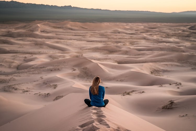 foto de mulher de costas sentada em dunas do deserto