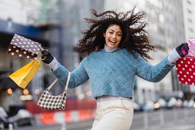 Foto de mulher de suéter azul segurando sacolas de compra