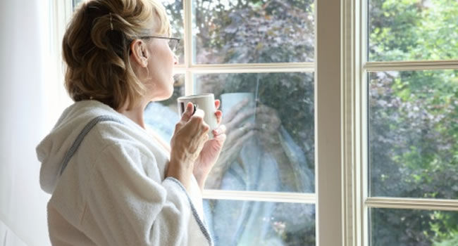 Mulher pensativa tomando chá e olhando pela janela