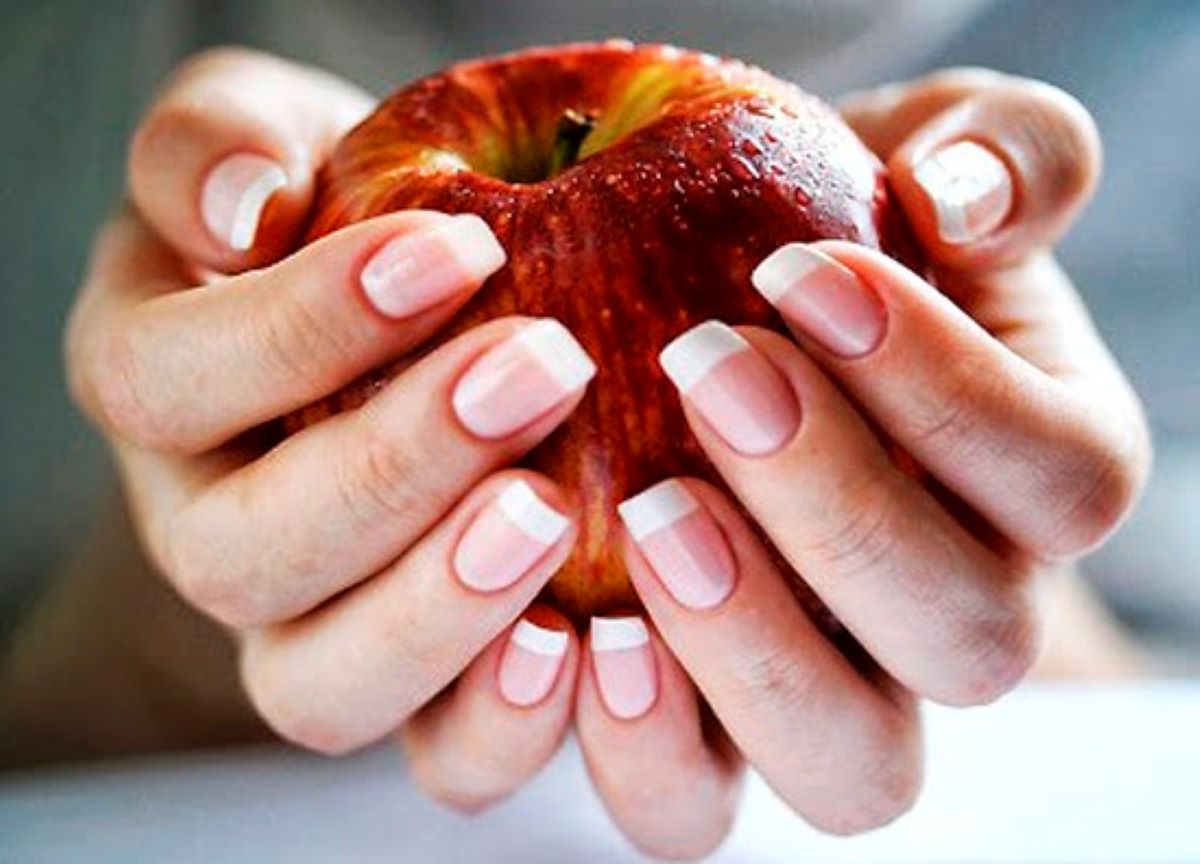 Mãos segurando uma maçã com foco para as unhas saudáveis