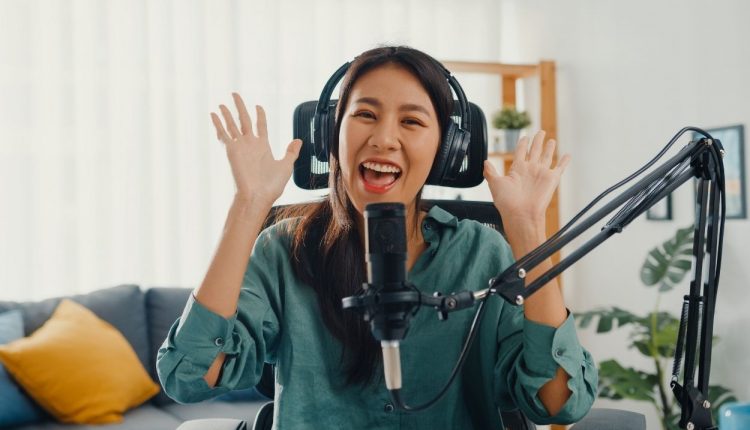 Menina asiática feliz gravando um podcast com fones de ouvido e microfone Imagem de uma apresentadora de podcast.