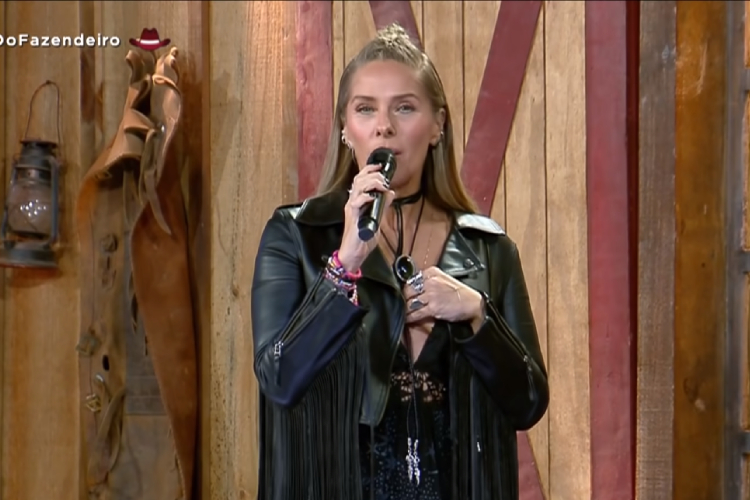 A imagem mostra a apresentadora Adriane Galisteu ao apresentar o reality. Ela usa uma jaqueta de couro preta. A Fazenda 2021 Programação 24/09