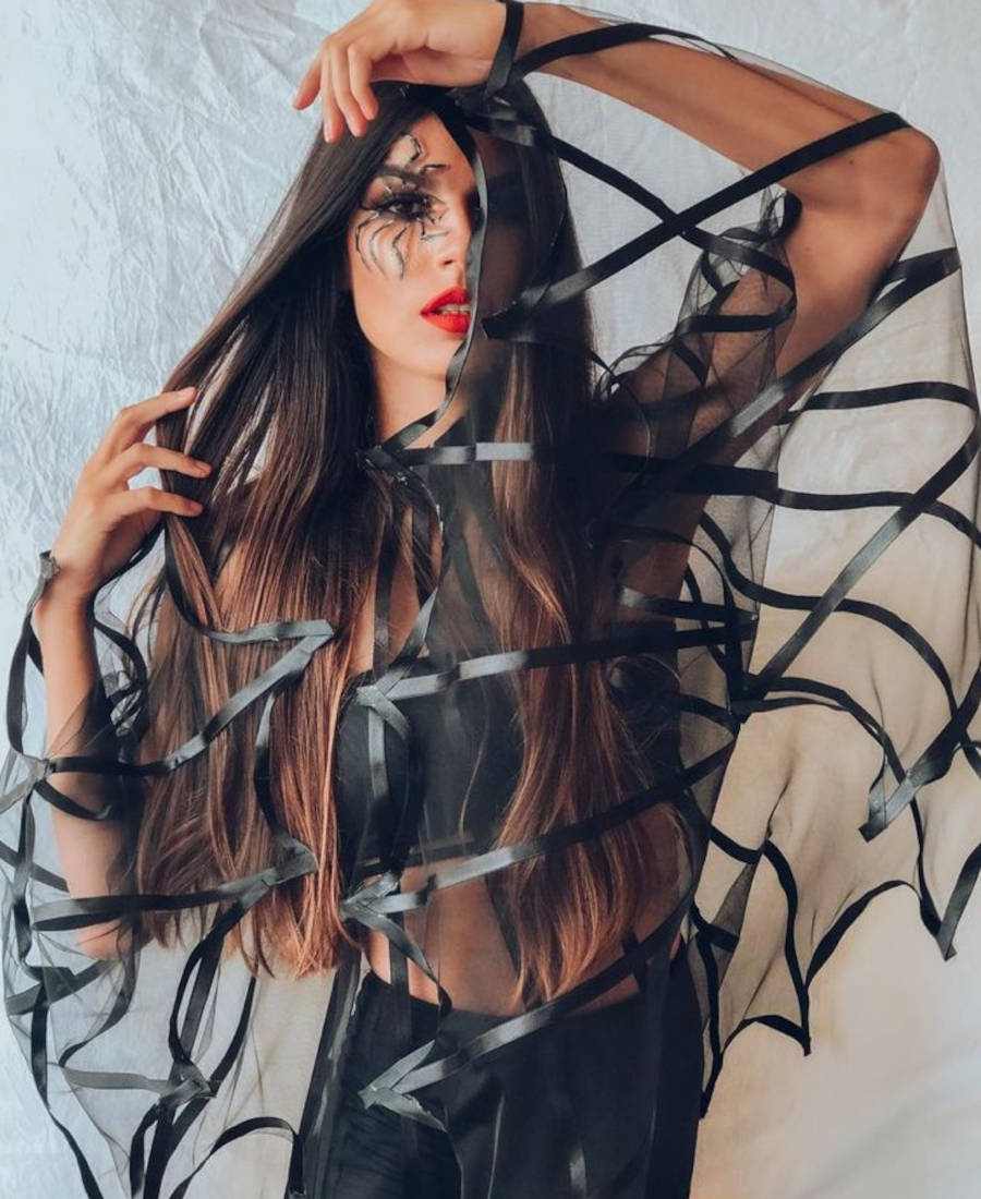 Foto de modelo posando com fantasia de aranha, com capa de aranha e maquiagem de aranha para o Halloween