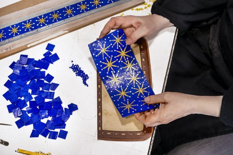Mão segurando detalhe de mosaico em azul e dourado 
