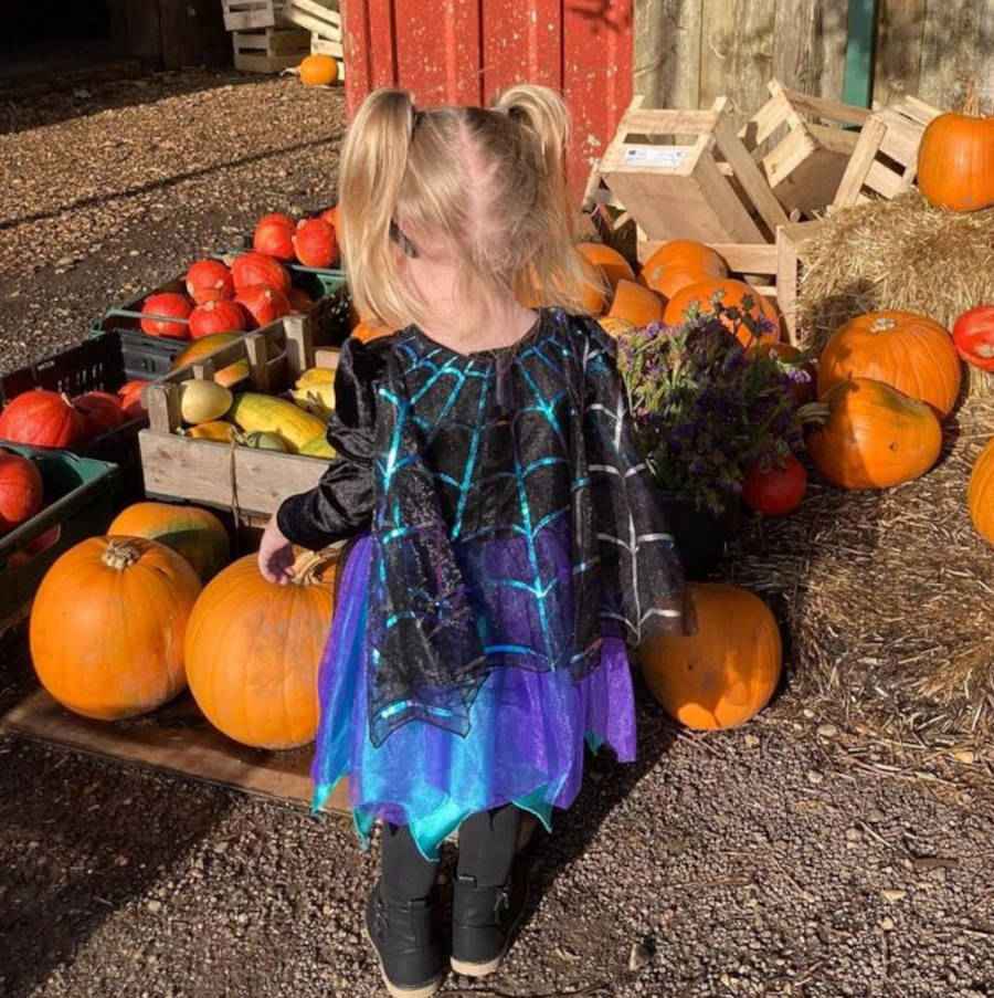 Imagem de uma criança de costas brincando com abóboras e fantasiada de aranha para o Halloween
