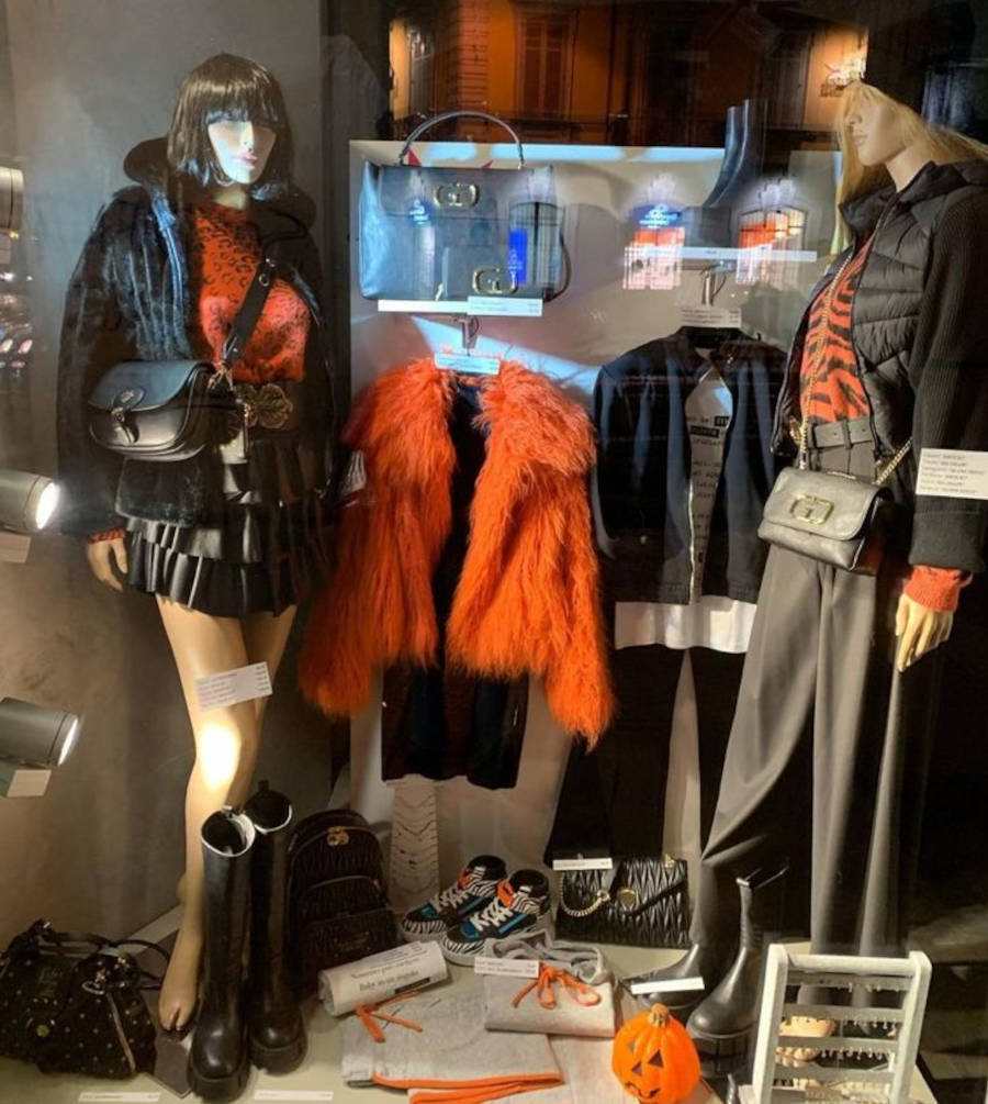 Foto de vitrine de loja de roupa decorada para o Halloween com peças em tons laranja e preto