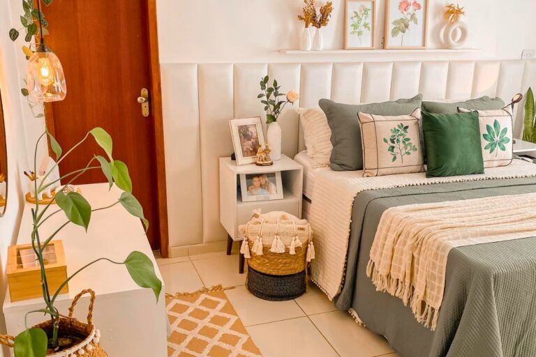 A imagem mostra um quarto decorado de forma simples e acolhedora. Há uma cama com lençóis cinza e almofadas verdes, um tapete bege com padrão geométrico, uma planta verde em um cesto, uma luminária pendente e pequenos objetos decorativos que criam um ambiente harmonioso e convidativo.