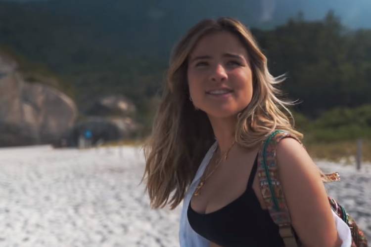 Print do clipe de Menina Solta, de Giulia Be. Ela aparece de cabelo solto, na praia e sorrindo. menina solta, giulia be