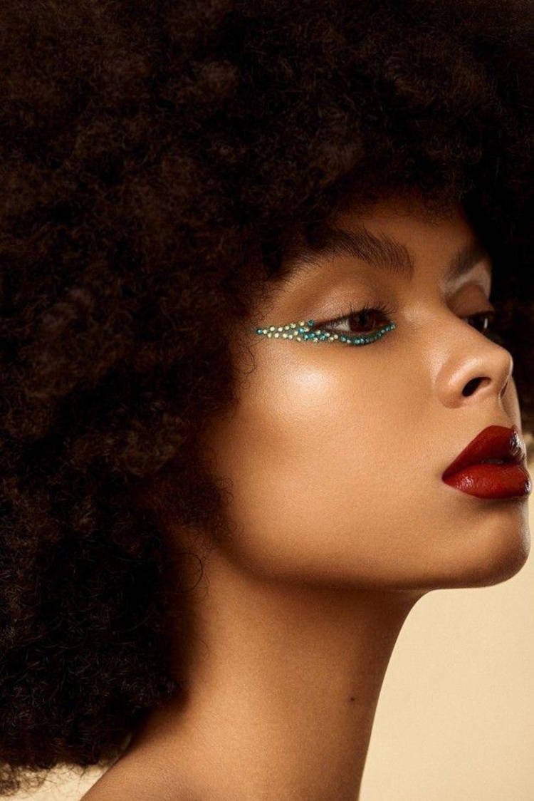 Mulher de pele morena usando delineado invertido com strass prata e azul, além de batom vermelho