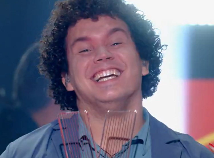 Giuliano sorri, com o troféu em mãos. Ele tem cabelo enrolado e usa blusa azul. Final The Voice Brasil: Giuliano Eriston é o campeão