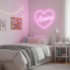 Um quarto delicado em tons de rosa e branco. A cama tem uma colcha branca de bolinhas e uma manta cinza. Acima da cama, um letreiro de néon em forma de coração rosa com o nome "Aurora" é o destaque.