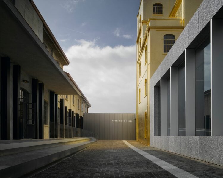 Foto mostra o corredor de entrada da Fundação Prada com edifícios em tom de prateado e dourado