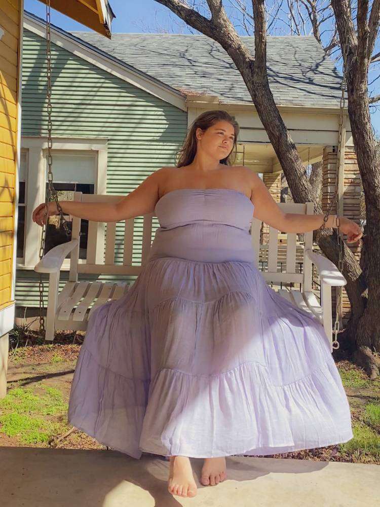 Mulher de pele clara sentada em balanço usando vestido longo tomara que caia lilás pastel