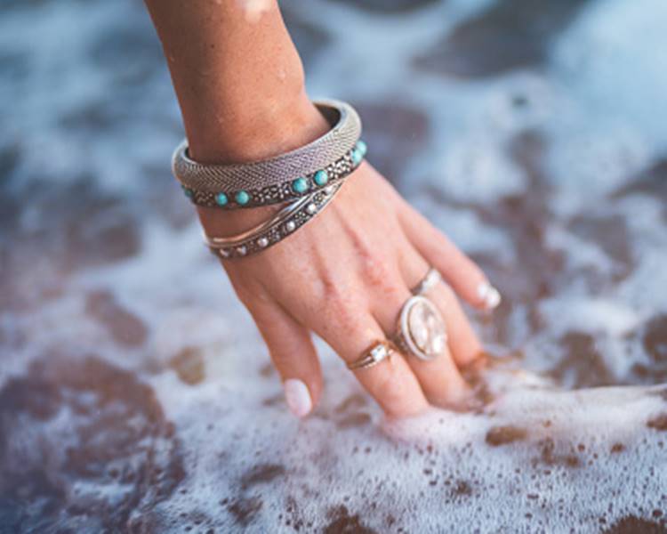 Foto de mão com joias na água do mar.