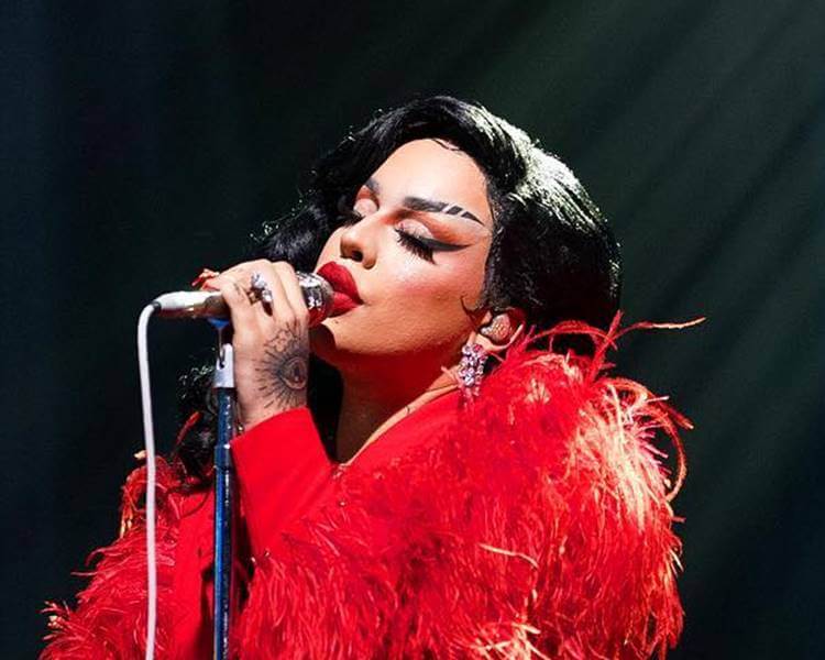 Drag queen Gloria Groove cantando em microfone. Foto da drag queen.