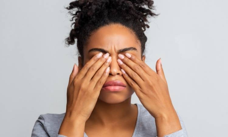Mulher coçando os olhos, causa do derrame ocular.