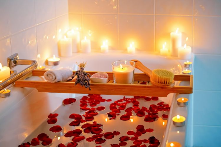 Banheiro com velas, banheira com pétalas de rosas e mesa de madeira com especiarias, toalha e escova