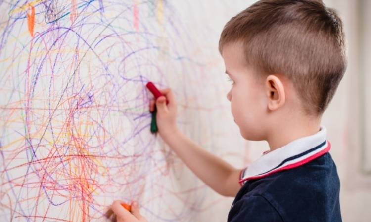 Criança desenhando com giz na parede.