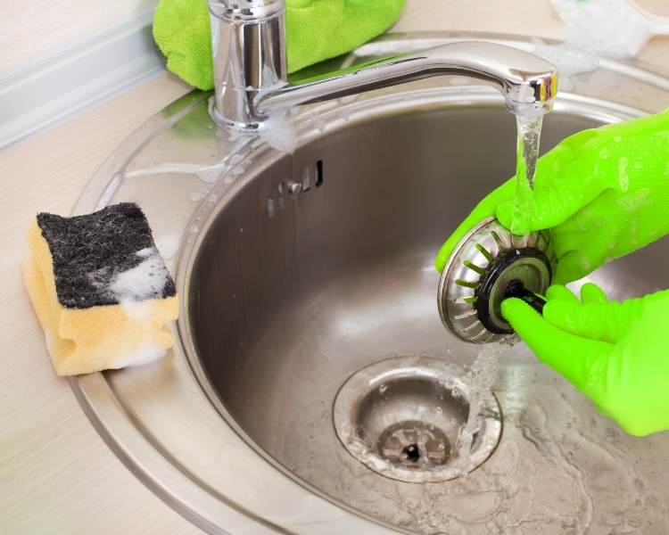 Foto de pessoa limpando pia com vinagre para limpeza.