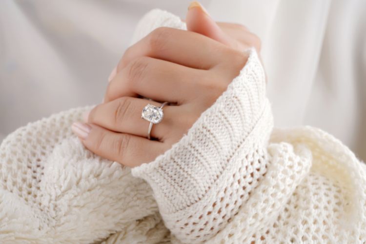 Mão de mulher segurando cobertor felpudo. Ela usa anel de diamante e esmalte perolado