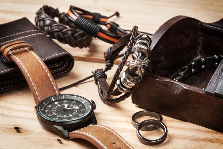 carteira, relógio, pulseiras e anéis masculinos dispostos em superfície de madeira