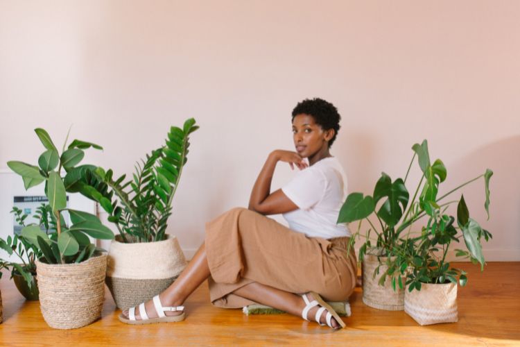 mulher sentada do lado de vasos de planta usando look de tons neutros e papete