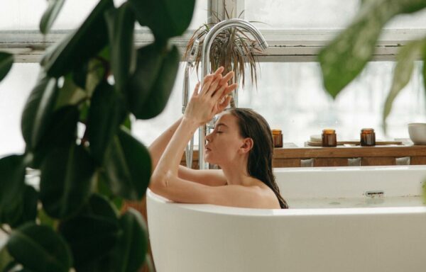 Banho de 7 ervas, mulher em uma banheira branca, com as mãos para o alto em um banheiro cheio de plantas