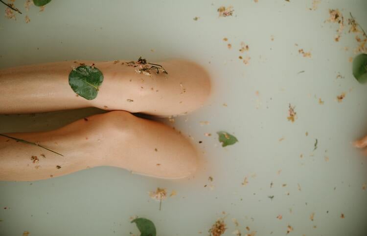 pernas de uma mulher em uma banheira com folhas de louro