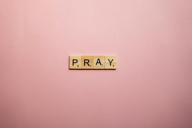 fundo rosa com as letras da palavra "PRAY" escritas em peças de madeira