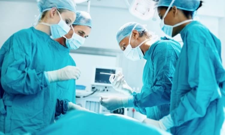 Equipe médica usando roupas cirúrgicas azuis, luvas, máscaras e tocas