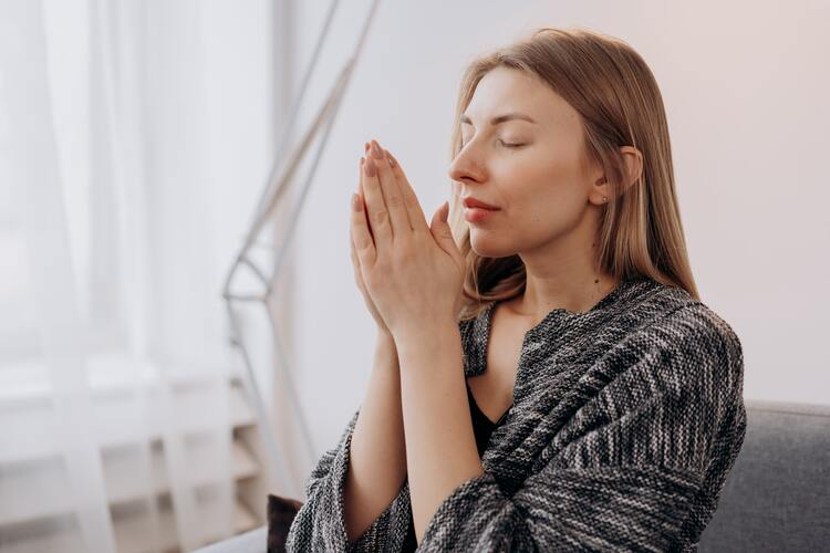 mulher branca com as mãos em fomra de oração e olhos fechados 