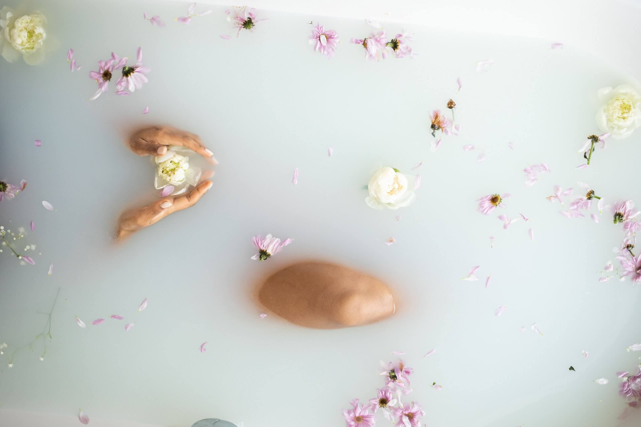 mulher tomando banho de banheira com rosas brancas e margaridas cor-de-rosa