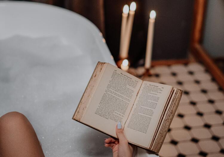 mulher tomando banho de banheira e lendo livro para renovar energias